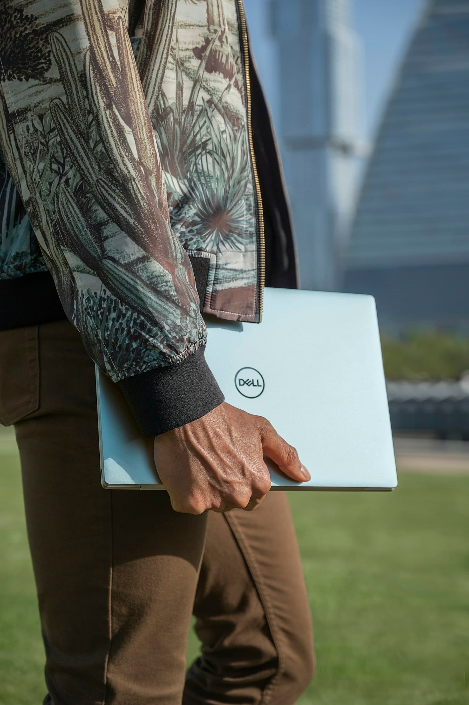 A person carrying a closed laptop outdoors