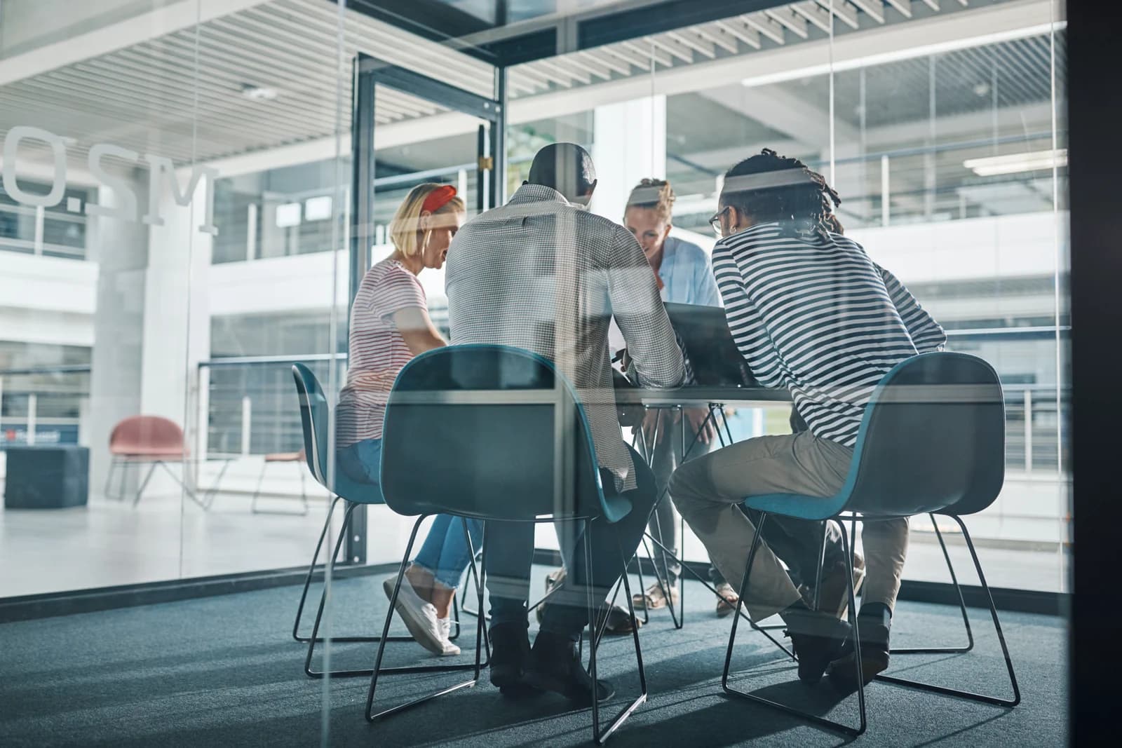 Four people meeting around a table in a glass-walled office